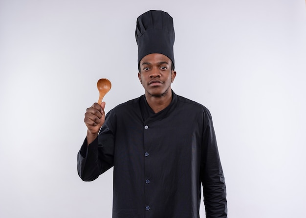 Photo gratuite jeune cuisinier afro-américain heureux en uniforme de chef détient une cuillère en bois isolé sur un mur blanc