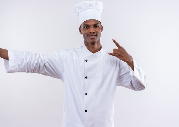 Jeune cuisinier afro-américain heureux en uniforme de chef gestes cornes avec main isolé sur mur blanc