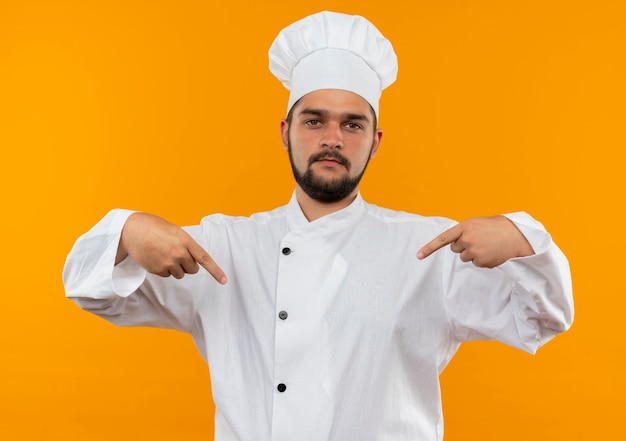 Jeune Cuisinier Confiant En Uniforme De Chef Pointant Sur Lui-même Isolé Sur Un Mur Orange