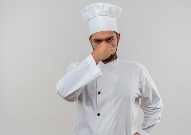 Jeune cuisinier irrité en uniforme de chef tenant le nez isolé sur un mur blanc avec espace de copie