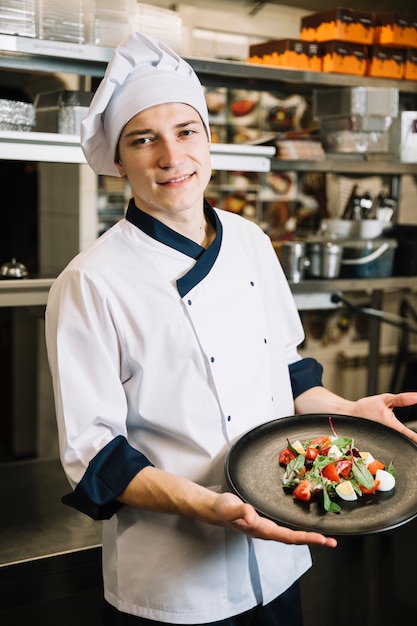 Jeune cuisinier tenant une assiette avec une salade végétarienne