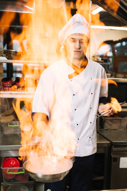Jeune cuisinier tenant une poêle en feu dans la main