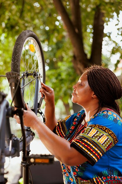 Jeune cycliste féminine active saisissant une clé pour serrer les vis et entretenir les pièces de vélo à l'extérieur. Femme afro-américaine enthousiaste sportive tenant un outil professionnel pour l'entretien du vélo à ho