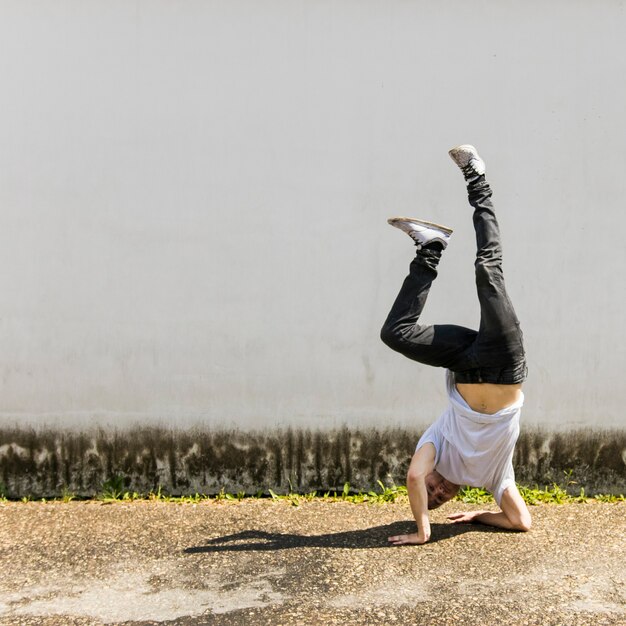 Photo gratuite jeune danseur faisant le poirier contre le mur gris