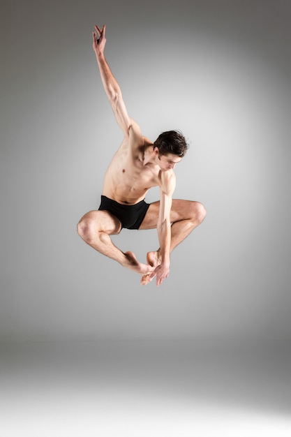 La jeune danseuse de ballet moderne attrayant sautant sur le mur blanc