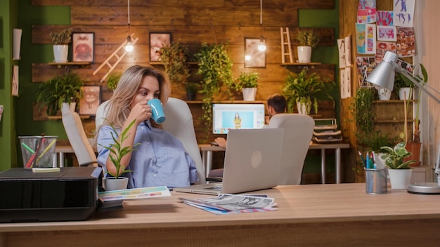 Jeune designer buvant du café et regardant l'ordinateur portable et a des impressions sur la table. Nouveau projet et travail d'équipe