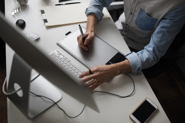 Jeune designer masculin à l'aide de tablette graphique tout en travaillant avec com