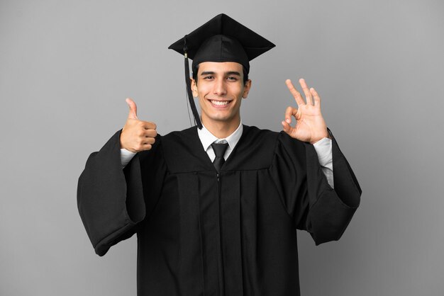 Jeune diplômé universitaire argentin isolé sur fond gris montrant le signe ok et le geste du pouce vers le haut