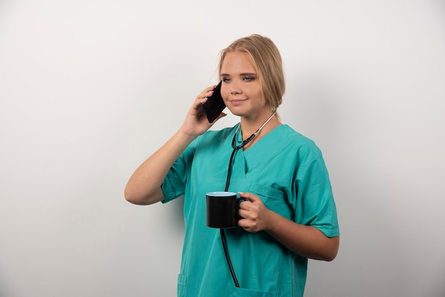 Jeune docteur tenant le thé tout en parlant avec le téléphone.