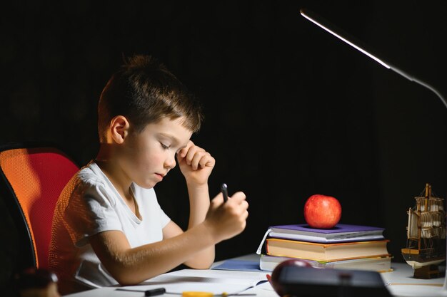 Jeune écolier adolescent à la table à faire ses devoirs dans la pièce sombre