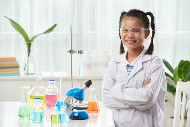 Jeune écolière asiatique qui pose en classe de chimie avec des flacons colorés