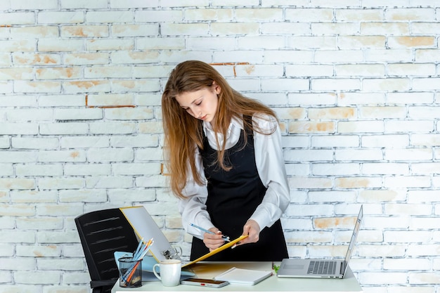 Photo gratuite jeune écolière assise derrière un bureau et écrivant des notes