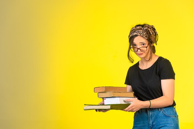 Jeune écolière à lunettes tenant ses livres et par-dessus ses lunettes.