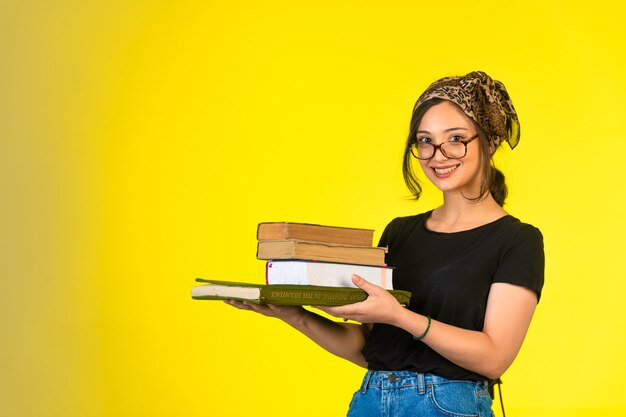 Jeune écolière à lunettes tenant ses livres et souriant positivement.