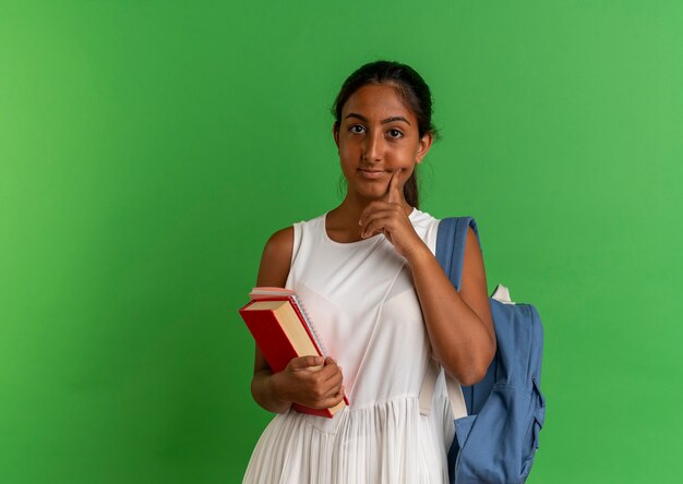 jeune écolière portant sac à dos tenant livre avec ordinateur portable mettant le doigt sur la joue