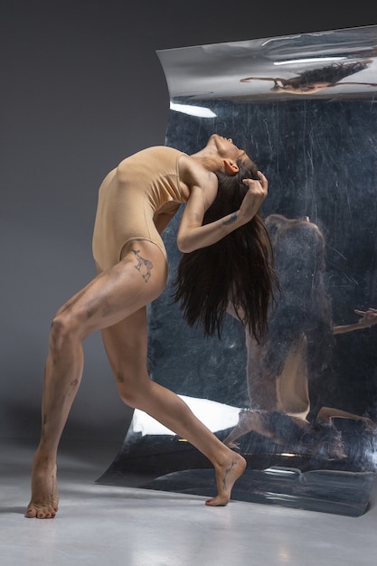 Jeune et élégant danseur de ballet moderne sur mur gris avec le miroir et les reflets d'illusion sur la surface