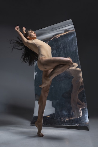 Jeune et élégant danseur de ballet moderne sur mur gris avec le miroir et les reflets d'illusion sur la surface