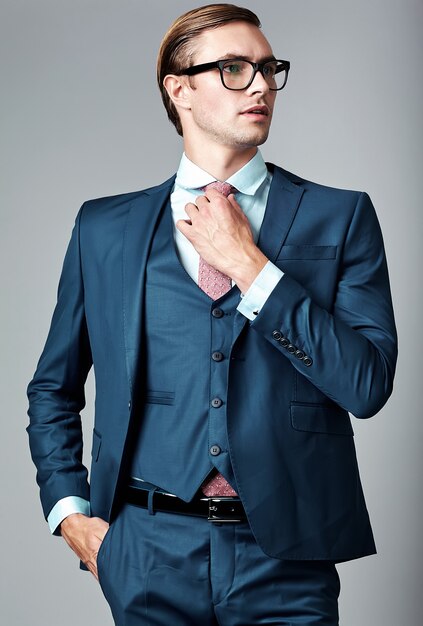 Jeune élégant modèle masculin beau homme d'affaires en costume bleu et lunettes à la mode, qui pose en studio