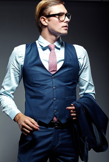 Jeune élégant modèle masculin beau homme d'affaires en costume bleu et lunettes à la mode, qui pose en studio