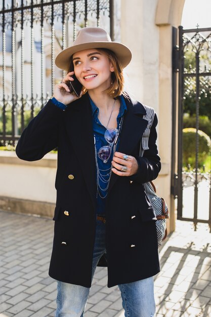 Jeune élégante jolie femme souriante et parler sur son téléphone, vêtue d'un manteau bleu foncé et d'un jean