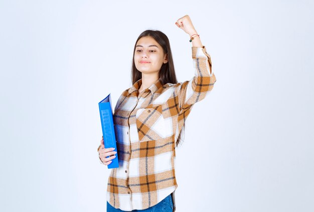 jeune employé tenant un dossier bleu sur un mur blanc.