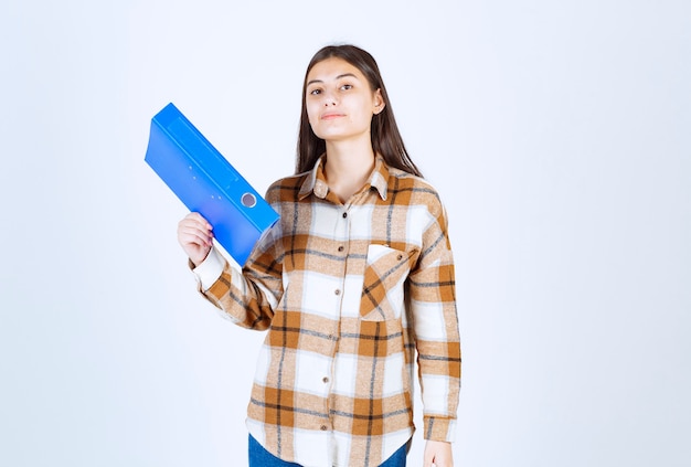 Jeune employée tenant un support bleu sur un mur blanc.