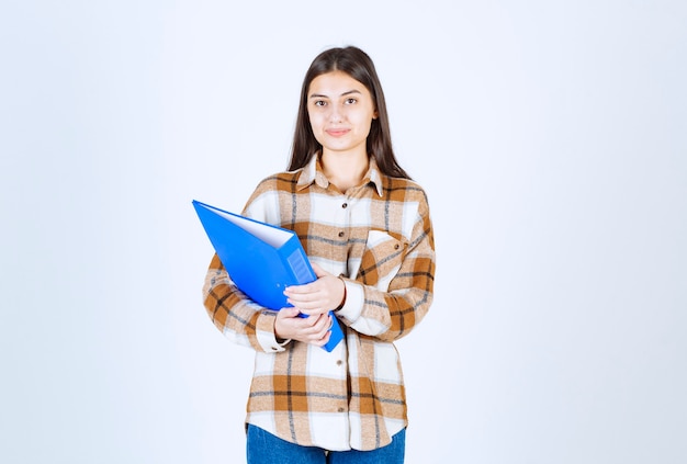 Jeune employée tenant un support bleu sur un mur blanc.