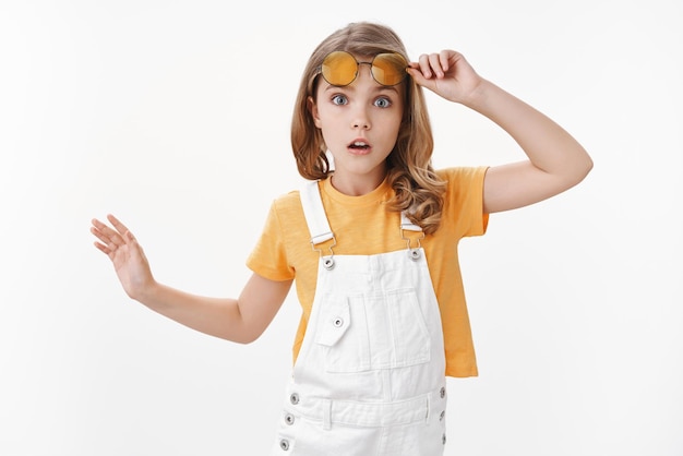 Jeune enfant assez à la mode, les lunettes de soleil jaunes élégantes au décollage ont l'air étonné et surpris