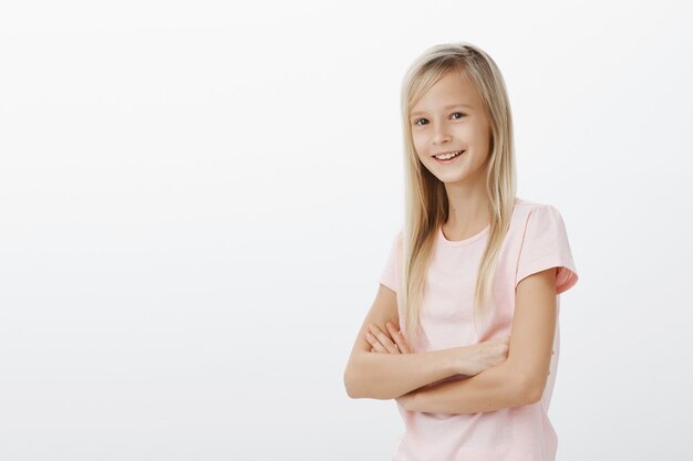 Jeune enfant souriant à la recherche de plaisir. Petite femme debout sur un mur blanc joyeux