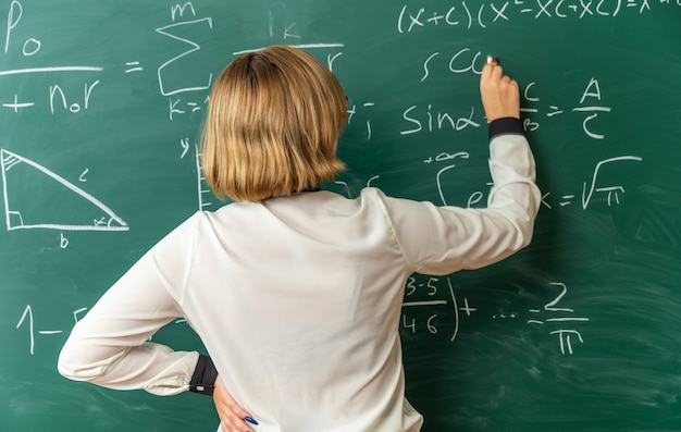 Jeune enseignante debout devant le tableau noir écrit quelque chose sur le tableau noir avec échoué pour le conseil en classe