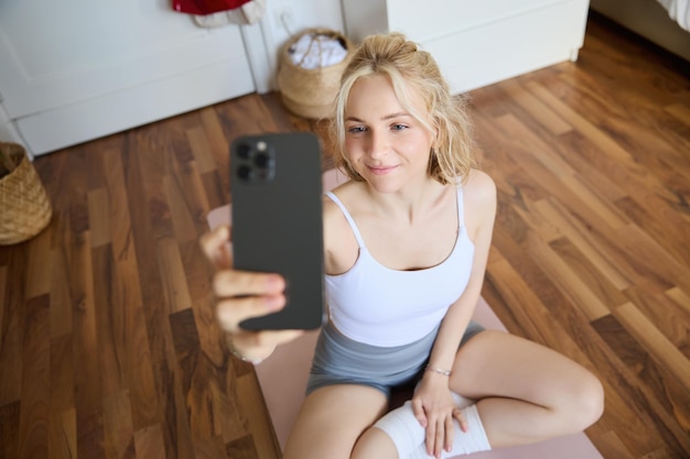 Photo gratuite jeune entraîneur de fitness sportif instructeur de yoga fait une diffusion en direct prend des selfies sur son smartphone pendant