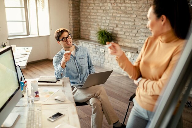 Jeune entrepreneur communiquant avec une collègue qui présente un plan d'affaires sur un tableau blanc