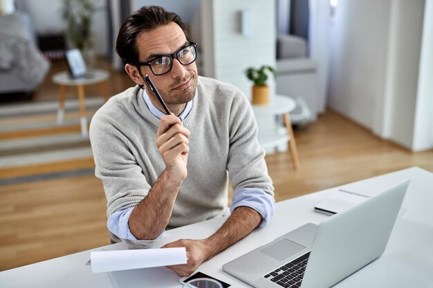 Jeune entrepreneur pensant tout en travaillant sur des rapports d'activité à la maison