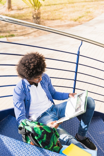 Jeune étudiant africain assis sur un escalier en lisant le livre