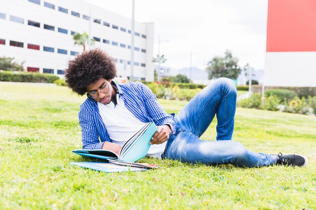 Jeune étudiant afro-africain, couché sur l&#39;herbe verte, lisant le livre