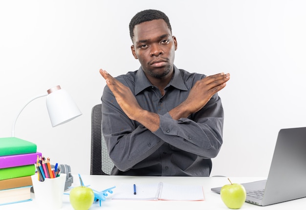 Jeune étudiant afro-américain confiant assis au bureau avec des outils scolaires croisant ses mains ne faisant aucun signe