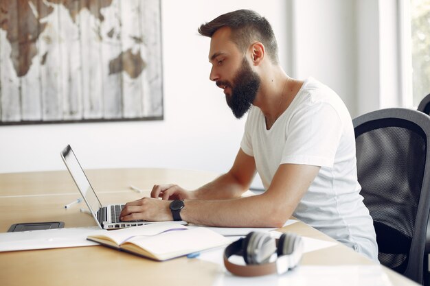 Jeune étudiant assis à la table et utilise son ordinateur portable