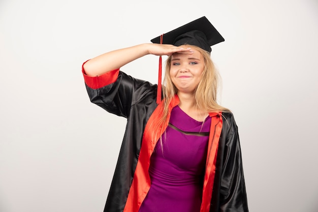 Jeune étudiant diplômé en robe se sentant heureux sur blanc.