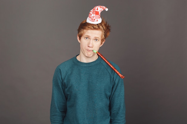 Jeune étudiant mâle malheureux avec des cheveux courts au gingembre dans un pull vert décontracté et un chapeau de Noël