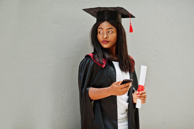 Jeune étudiante afro-américaine avec diplôme et pose de téléphone portable à l'extérieurxA