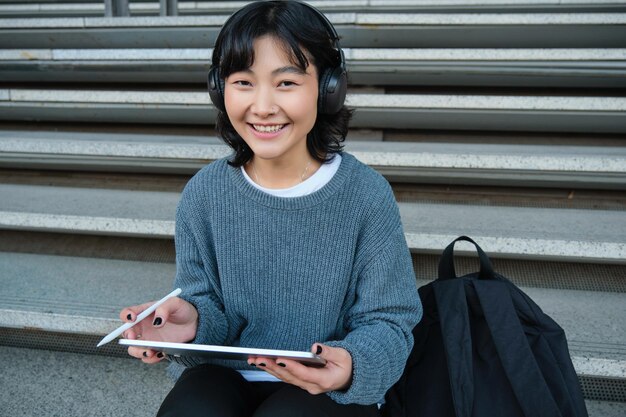 Une jeune étudiante asiatique dans un casque travaille sur un artiste numérique à distance dessinant sur une tablette avec un graphique