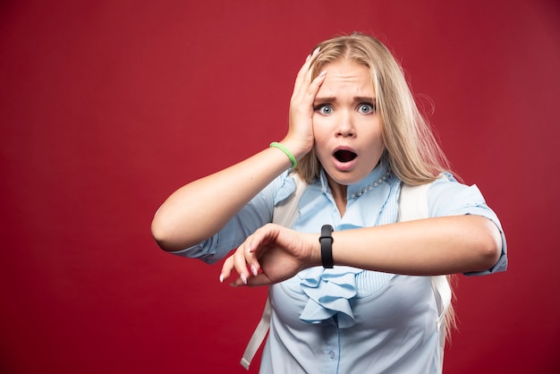 Photo gratuite une jeune étudiante blonde retourne à l'école, vérifie l'heure et est stressée car elle est en retard.