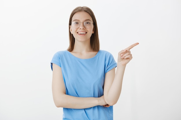 Jeune étudiante dans des verres souriant et pointant le doigt à droite, à la recherche d'intrigué