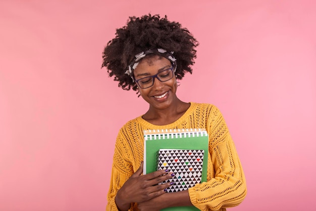 Photo gratuite jeune étudiante dans des verres tenant des livres à la main isolé sur fond rose portrait quotidien décontracté étudiant tenant des cahiers souriant