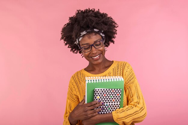 Jeune étudiante dans des verres tenant des livres à la main isolé sur fond rose portrait quotidien décontracté étudiant tenant des cahiers souriant