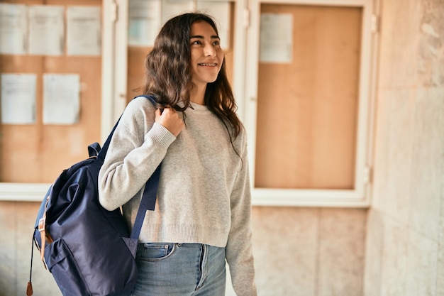 Jeune étudiante du moyen-orient souriante heureuse tenant un livre à la ville.