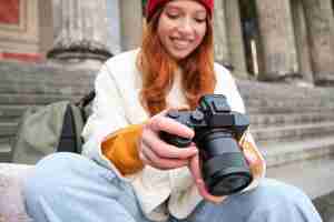 Photo gratuite une jeune étudiante photographe est assise dans les escaliers de la rue et vérifie ses prises de vue sur un appareil photo professionnel