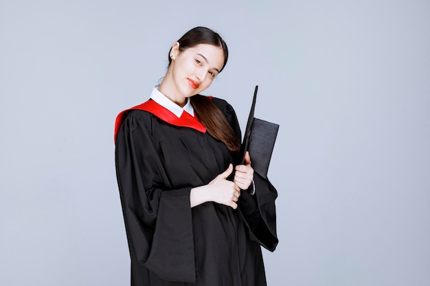 Jeune étudiante en robe tenant une casquette et posant. photo de haute qualité