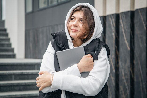 Une jeune étudiante se tient debout avec une tablette numérique dans les mains à l'extérieur