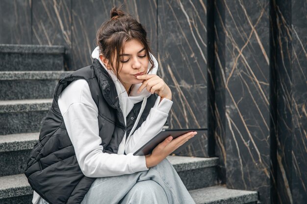 Une jeune étudiante se tient debout avec une tablette numérique dans les mains à l'extérieur